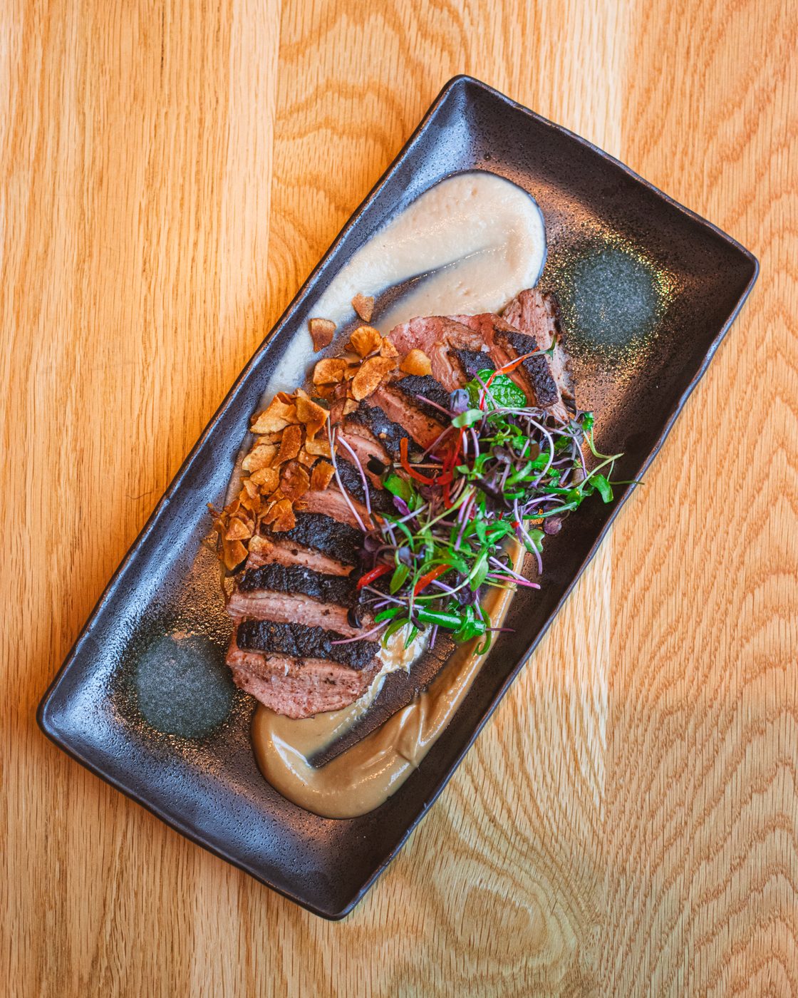 Sliced steak with mushrooms and sauce on a dark platter